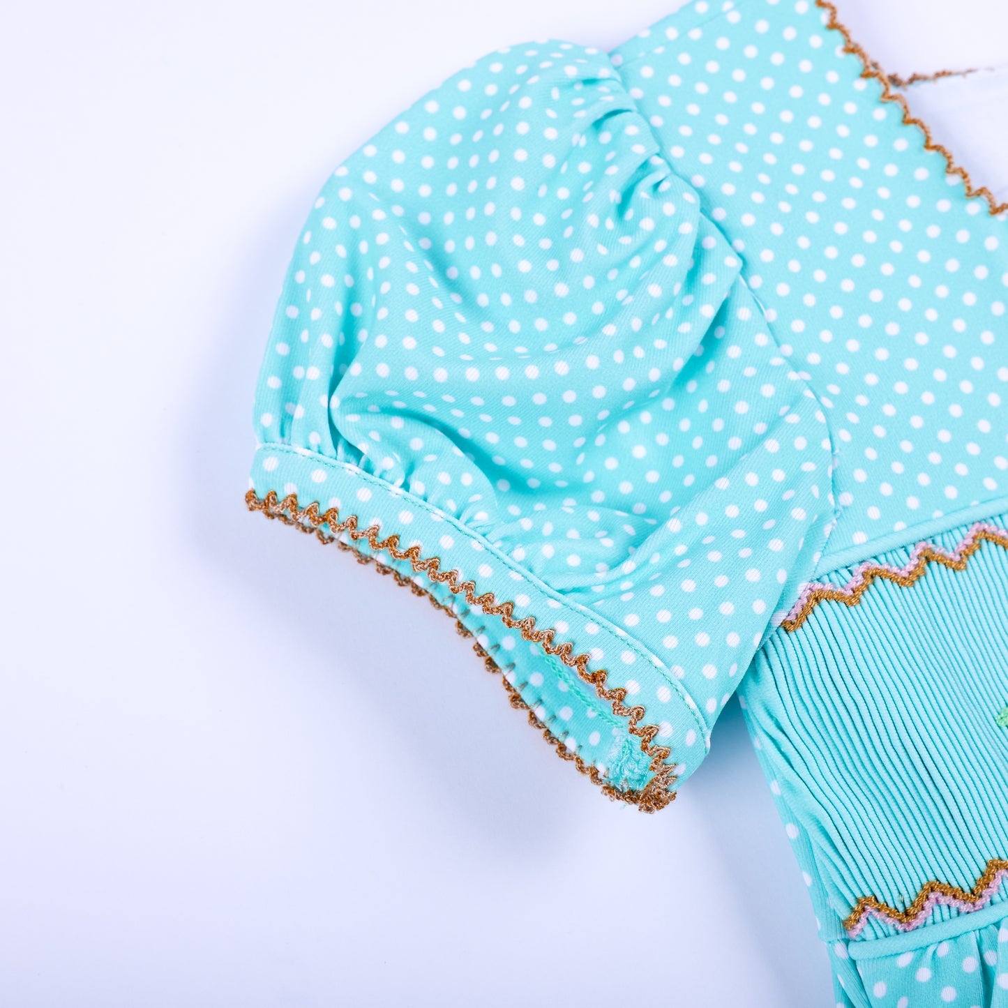 Detailed close-up view of puffed sleeve with gold picot trim on aqua polka dot hand smocked girls outfit.