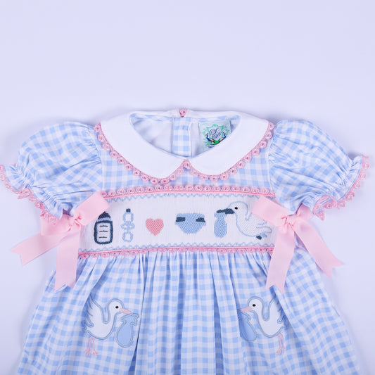 Mid shot of hand smocked baby shower announcement dress showing embroidered motifs, pink bows, and Peter Pan collar.