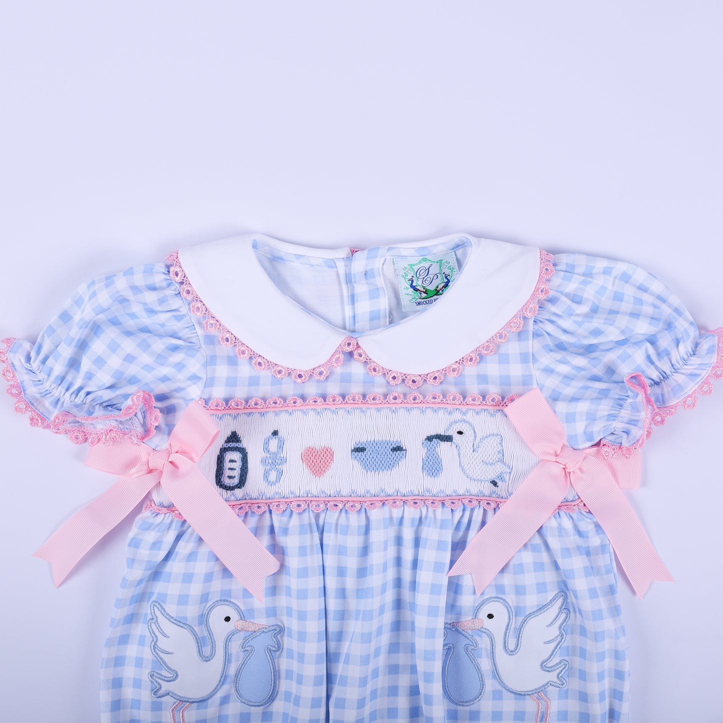 Upper view of the baby gender reveal smocked bubble romper showing the white Peter Pan collar and pink satin bows.