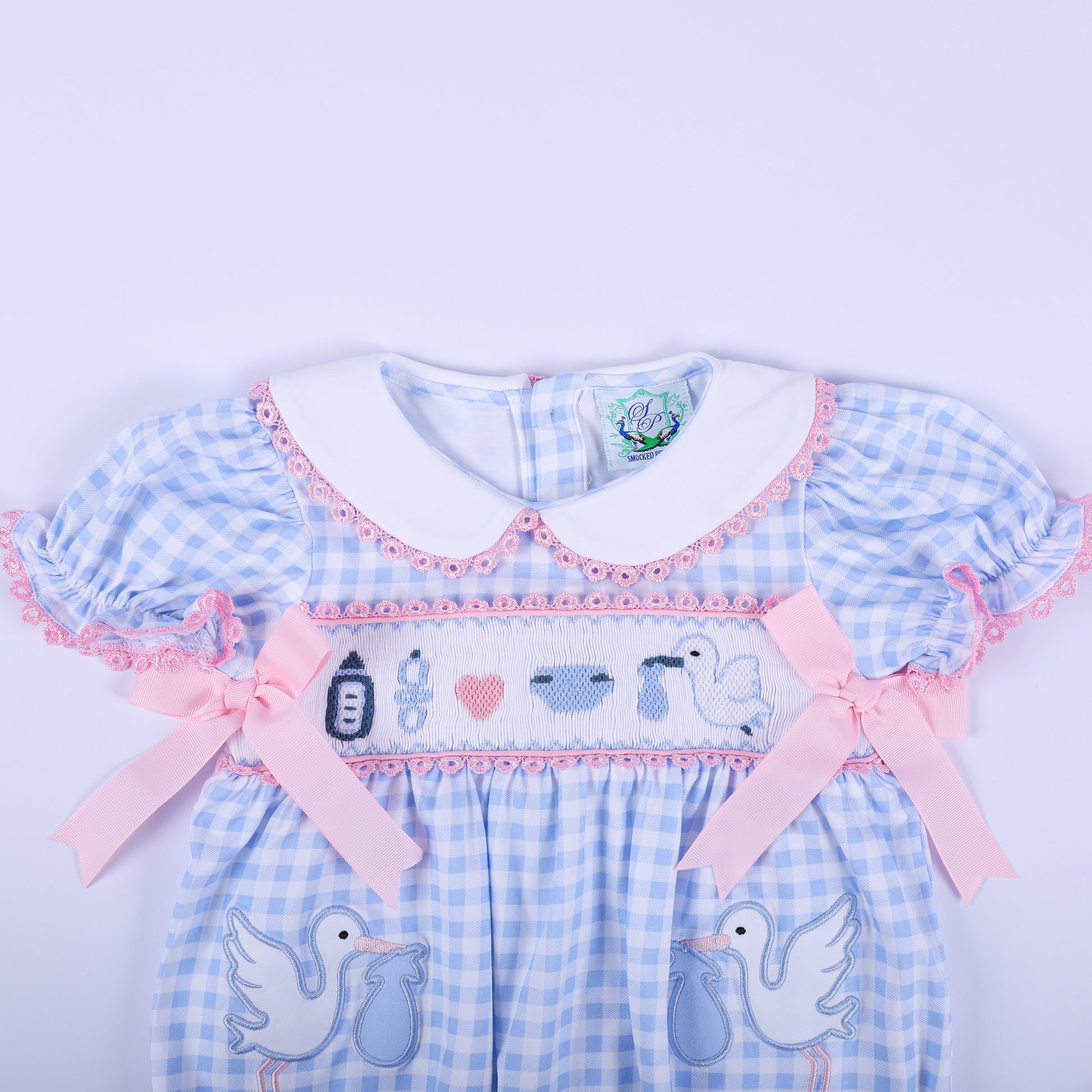 Upper view of the baby gender reveal smocked bubble romper showing the white Peter Pan collar and pink satin bows.