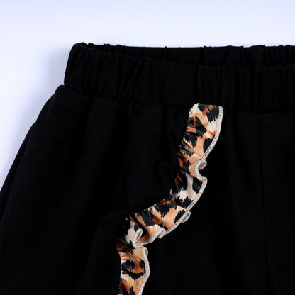 Close-up of elastic waistband and leopard print ruffle accent on toddler girls black smocked shorts.