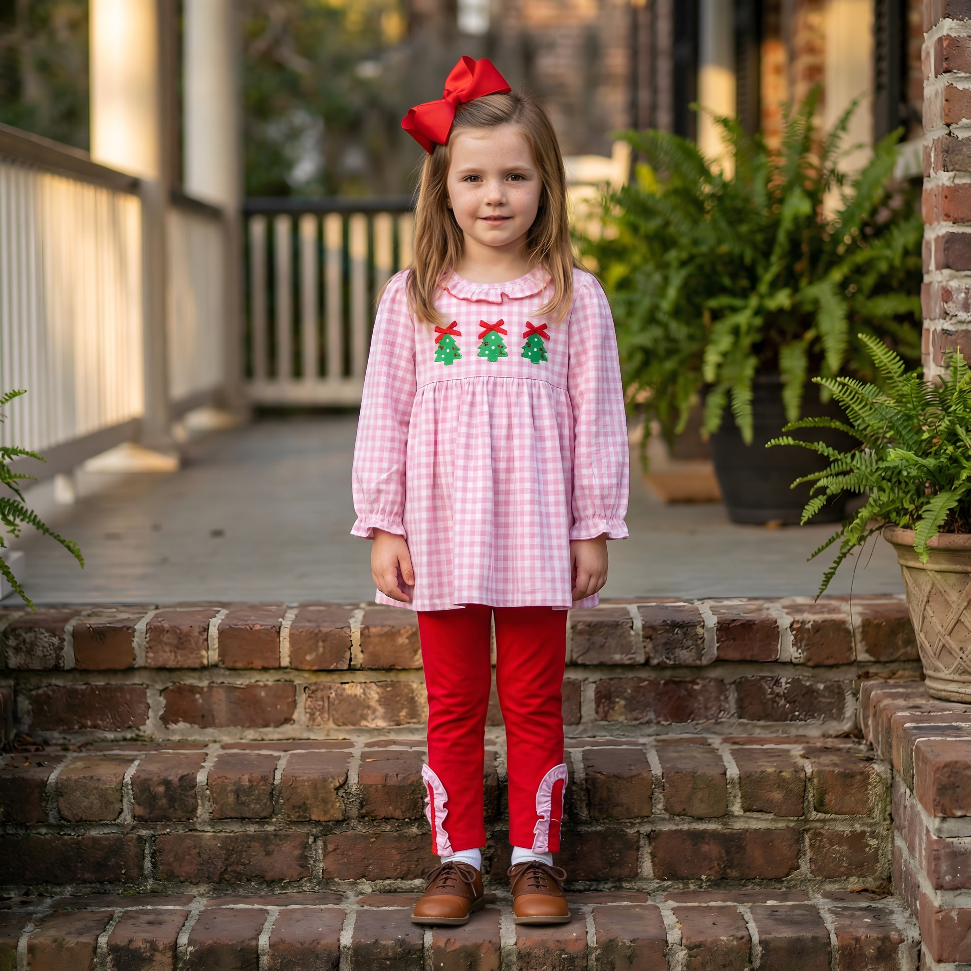 Girl in pink gingham smocked top with three Christmas trees and red ruffled pants from the Embroidered Christmas Tree Trio set.
