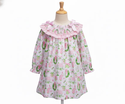 Girls watercolor smocked Christmas dress with pink collar bows and garland print displayed on a mannequin form.