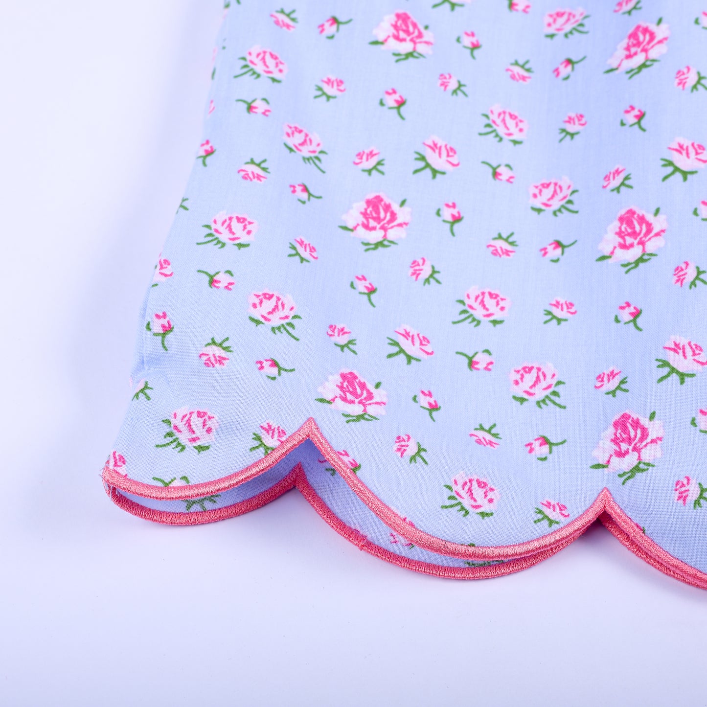 Detailed view of pink scalloped edged hem on light blue floral pattern hand-smocked dress for toddler girls.