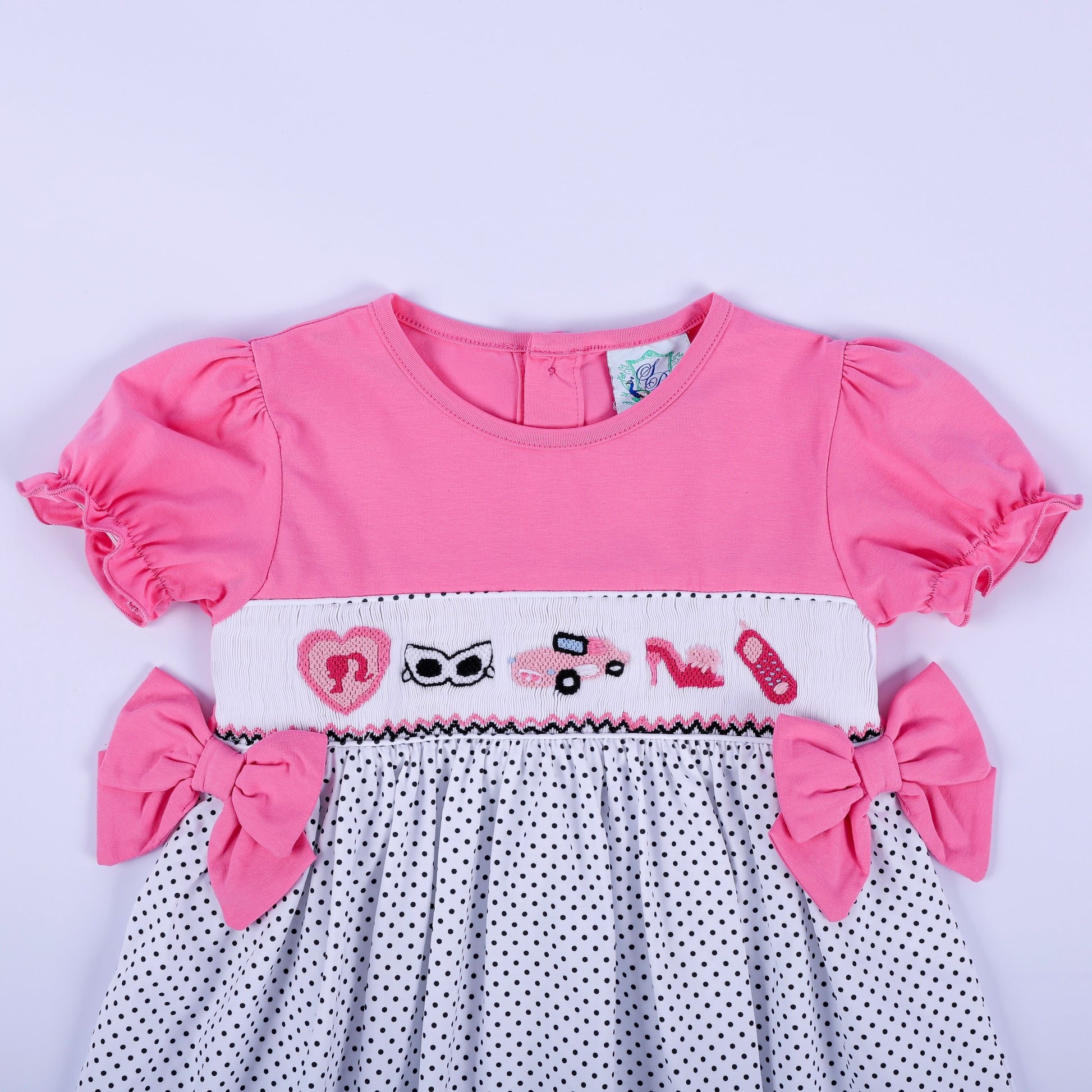 Close-up of hand embroidered fashion motifs on white hand smocked chest plate of girls pink polka dot dress.