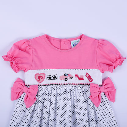 Close-up of hand embroidered fashion motifs on white hand smocked chest plate of girls pink polka dot dress.