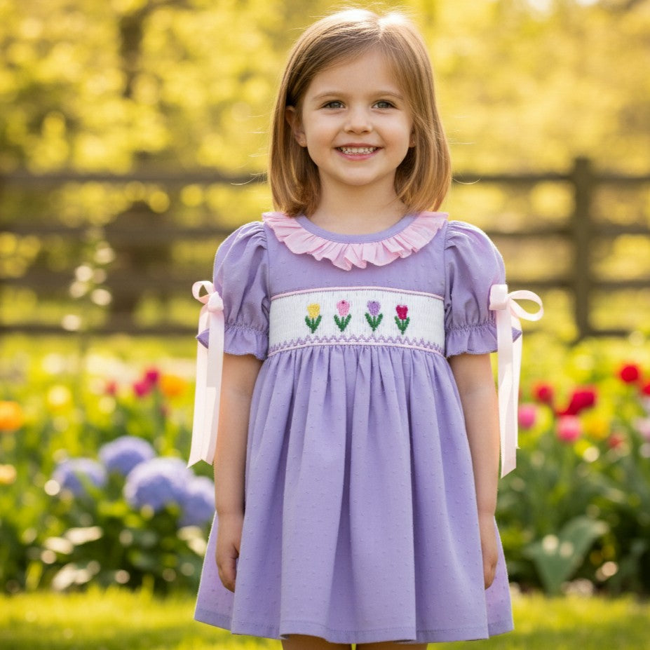 Smiling young girl wearing a lavender smocked spring dress with embroidered tulips and pink ruffled collar.