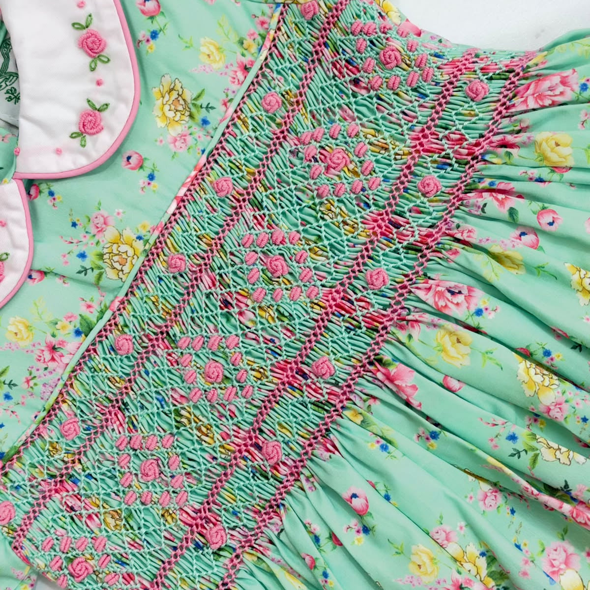 Close-up of hand-smocked mint green dress bodice with pink bullion rose embroidery