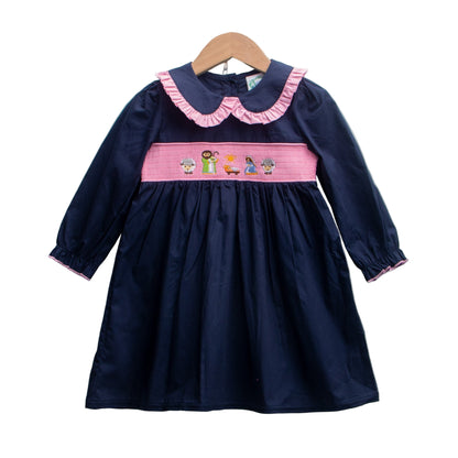 Girls navy blue smocked Christmas dress with a pink Peter Pan collar and embroidered nativity scene on the bodice panel.