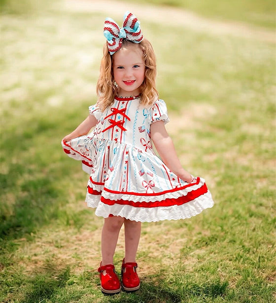 Little girl in a red, white, and blue 4th of July patriotic dress with ribbon bows and eyelet ruffle hem outdoors.