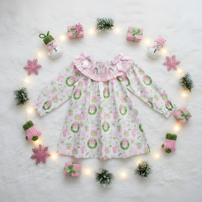 Top view flat lay of girls watercolor smocked Christmas dress styled with pink ornaments, string lights, and fur rug.
