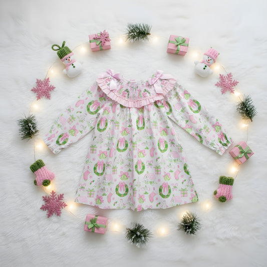 Top view flat lay of girls watercolor smocked Christmas dress styled with pink ornaments, string lights, and fur rug.