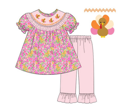 Two-piece girls Thanksgiving outfit featuring a pink and orange floral tunic top with smocked turkey details and matching light pink ruffle pants.