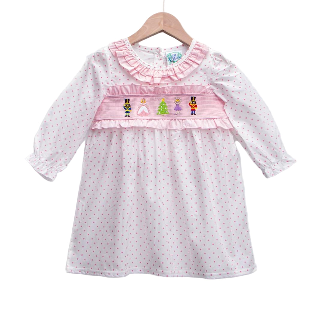Girls pink long sleeve smocked dress featuring embroidered Nutcracker figures and polka dots on a hanger.