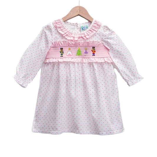 Girls pink long sleeve smocked dress featuring embroidered Nutcracker figures and polka dots on a hanger.