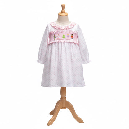 Girls pink Nutcracker smocked dress with polka dot pattern displayed on a wooden mannequin dress form.