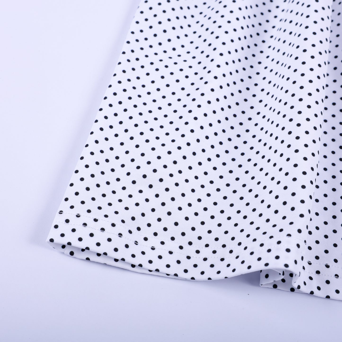 Close-up fabric detail of black and white polka dot skirt hem on girls fancy pink hand smocked dress.