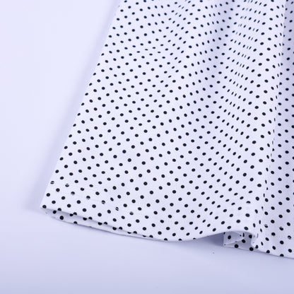 Close-up fabric detail of black and white polka dot skirt hem on girls fancy pink hand smocked dress.