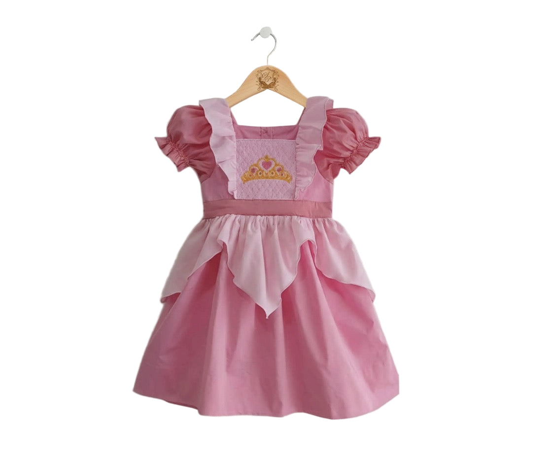 Pink kids princess dress featuring puff sleeves, a scalloped overlay, and an embroidered gold crown.