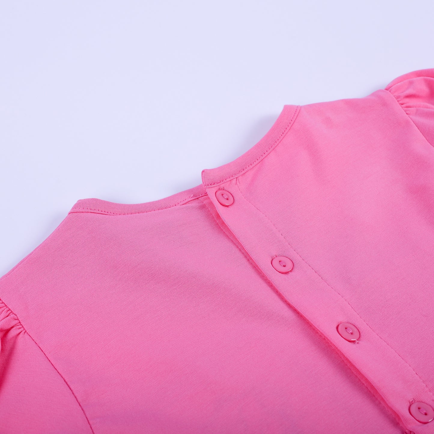 Close-up view of pink button closures on the back bodice of girls fancy hand smocked polka dot dress.