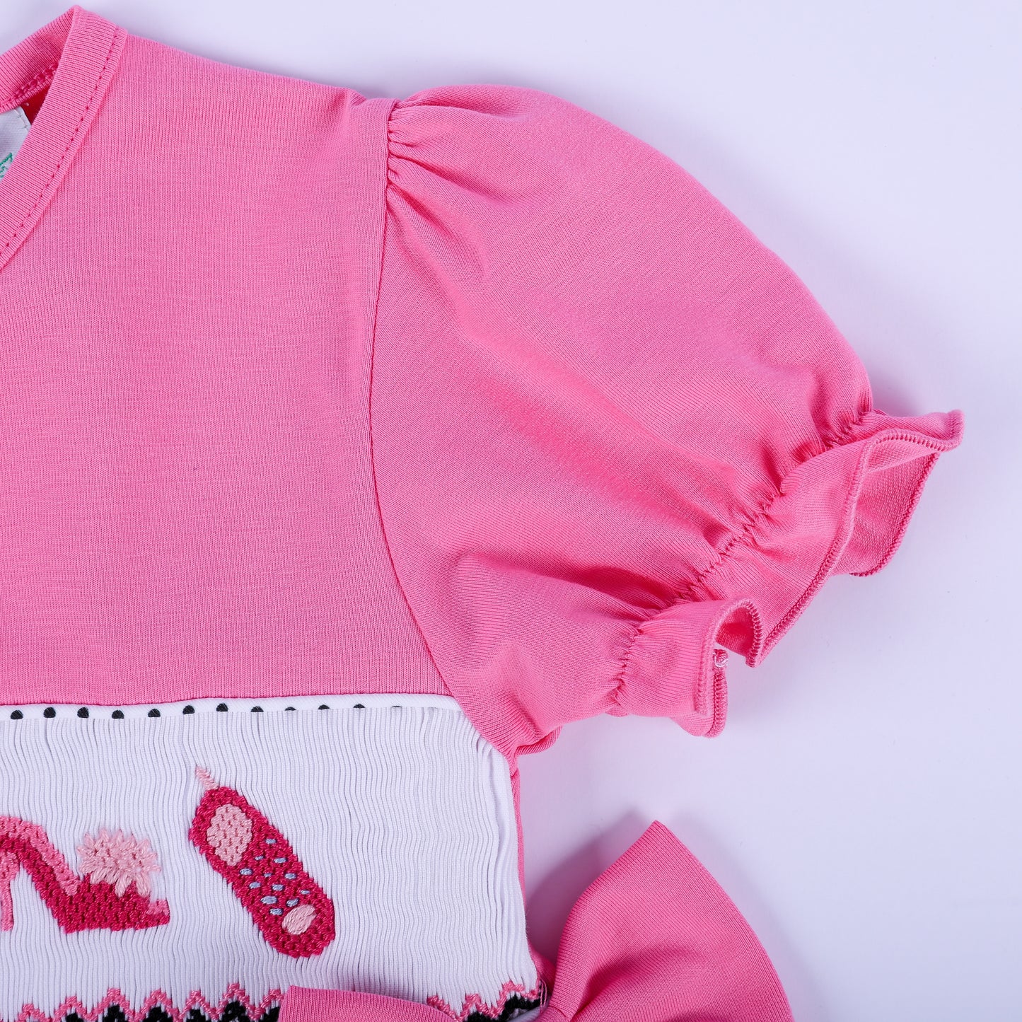 Detail view of ruffled pink puff sleeve and hand embroidered smocking on girls fancy polka dot dress.