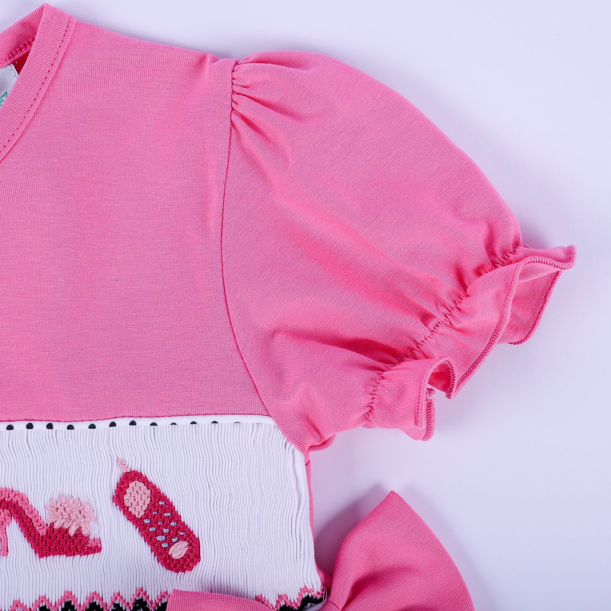 Detail view of ruffled pink puff sleeve and hand embroidered smocking on girls fancy polka dot dress.