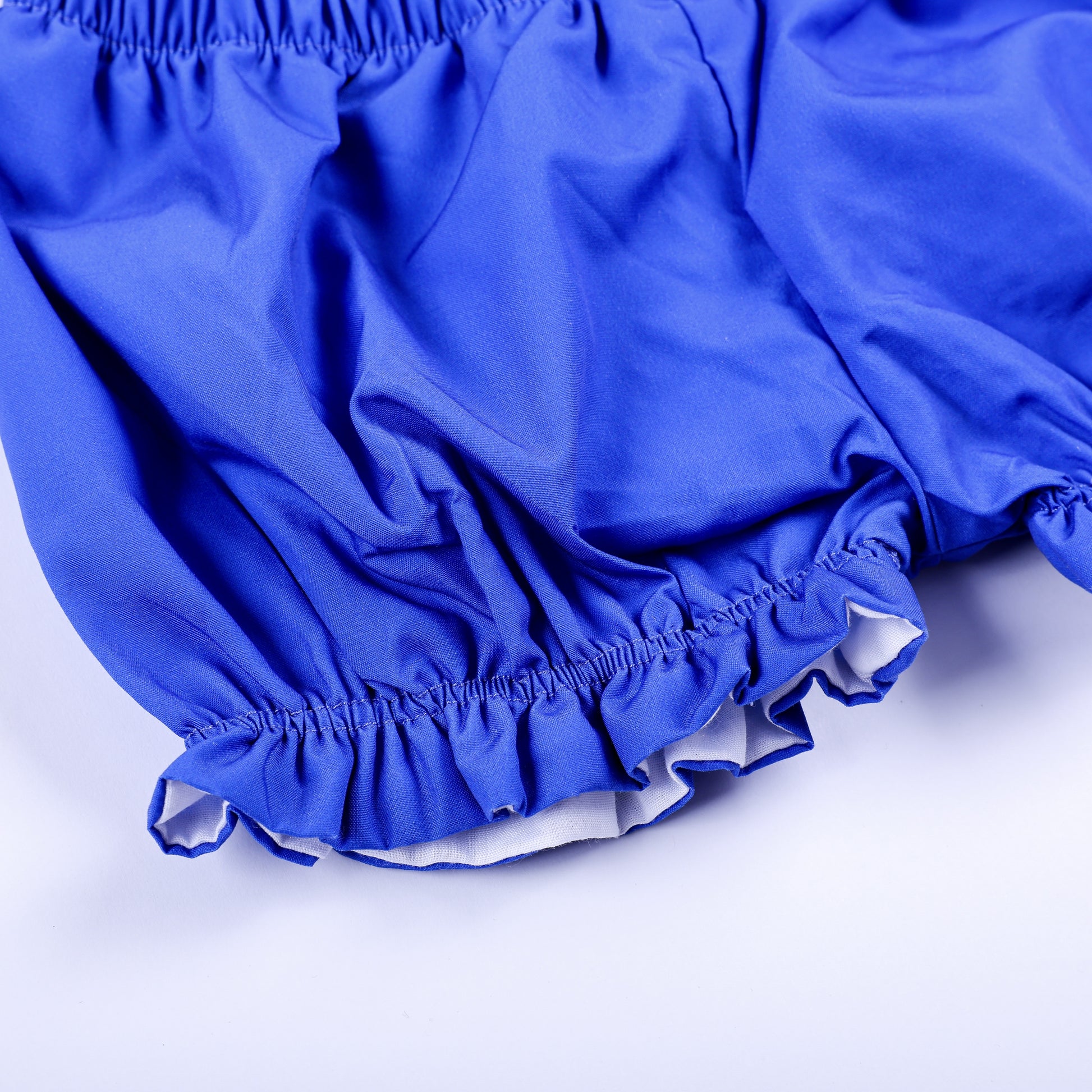 Close-up shot of elastic leg opening with delicate ruffle trim on girls royal blue smocked bloomer shorts.