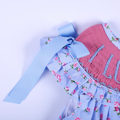 Detailed shot of light blue ribbon shoulder bow and ruffled sleeve on girls floral hand-smocked I Love Mom dress.