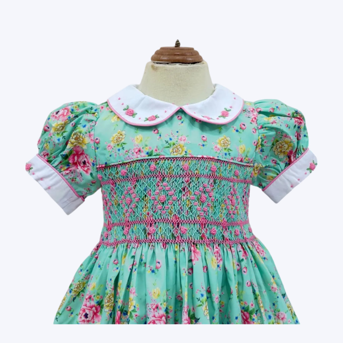Close-up mannequin view of hand-smocked bodice and collar on girls mint floral dress