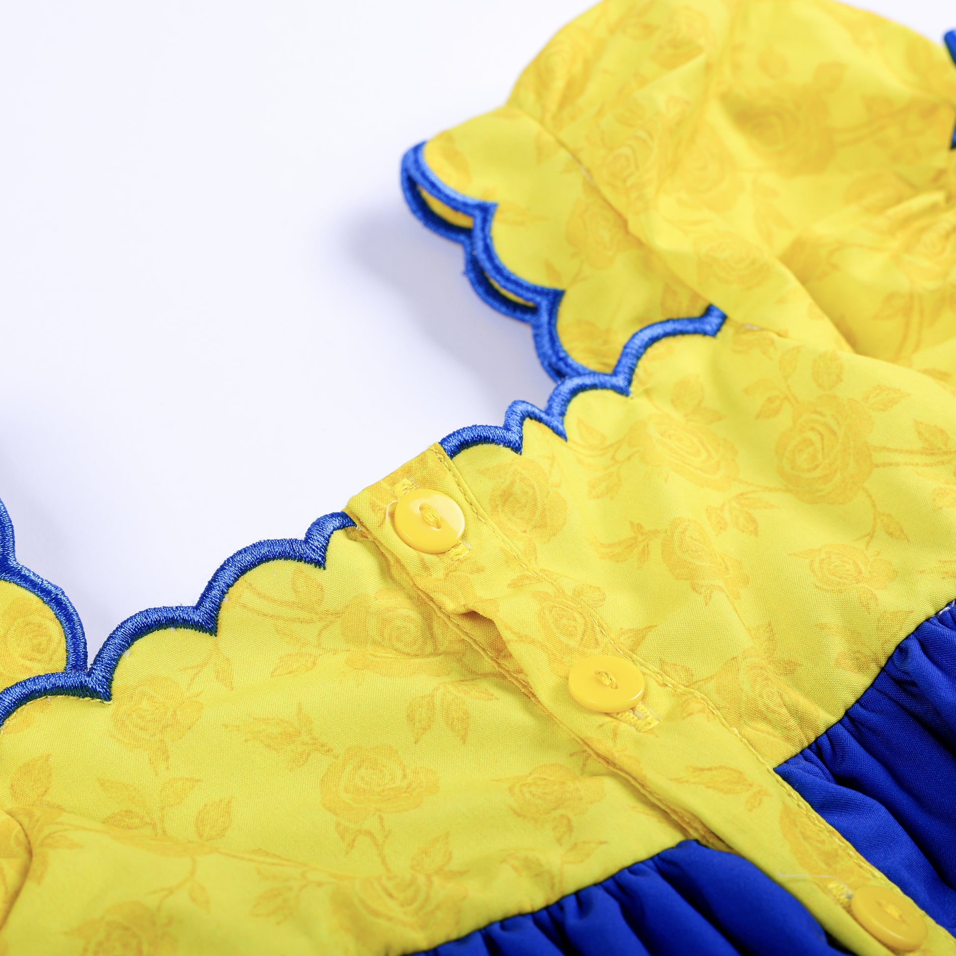 Close-up of yellow button placket closure and blue scalloped trim on back of girls fairytale smocked top.
