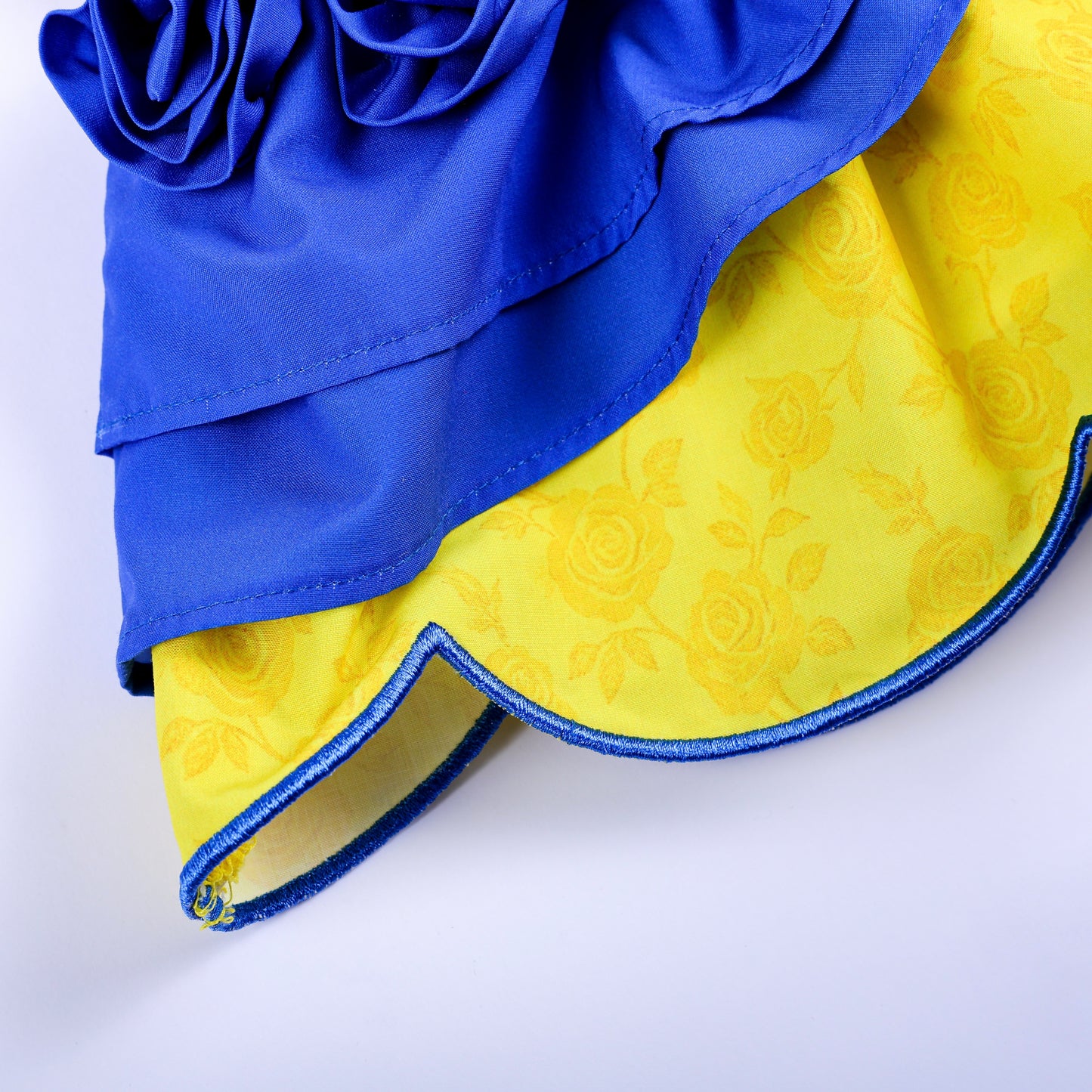 Detailed view of blue embroidered scalloped hem and yellow rose patterned fabric on girls smocked top.