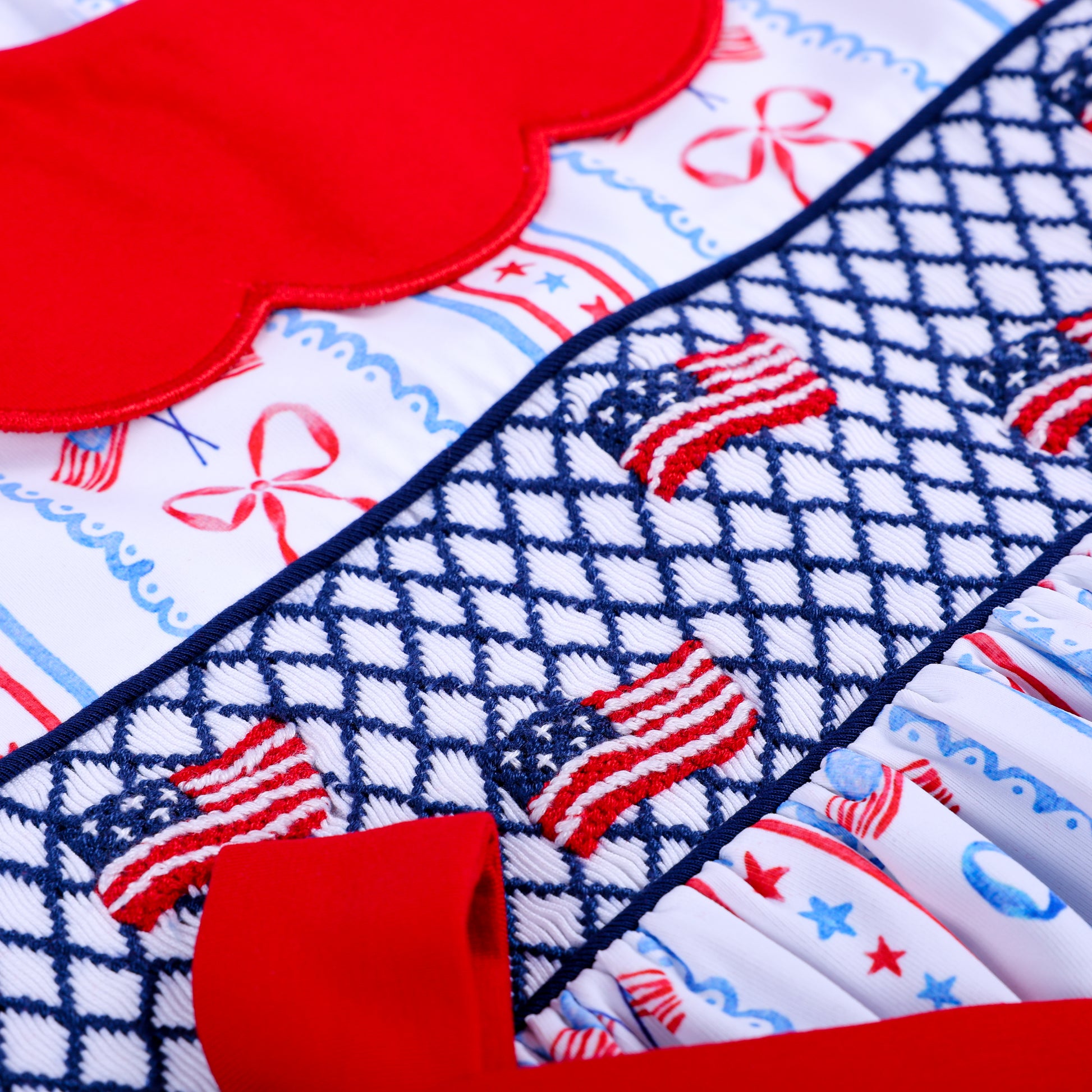 High detail shot of hand embroidered US flags on dark blue geometric smocking for patriotic toddler girl outfit.