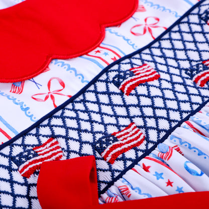High detail shot of hand embroidered US flags on dark blue geometric smocking for patriotic toddler girl outfit.