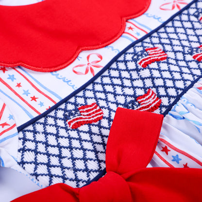 Macro view of hand-smocked navy grid with hand-embroidered American flags and red side bow on patriotic baby bubble.