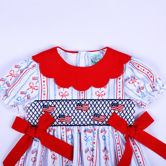 Close up of hand embroidered patriotic American flag smocking on a baby girl top with red scalloped collar and bows.