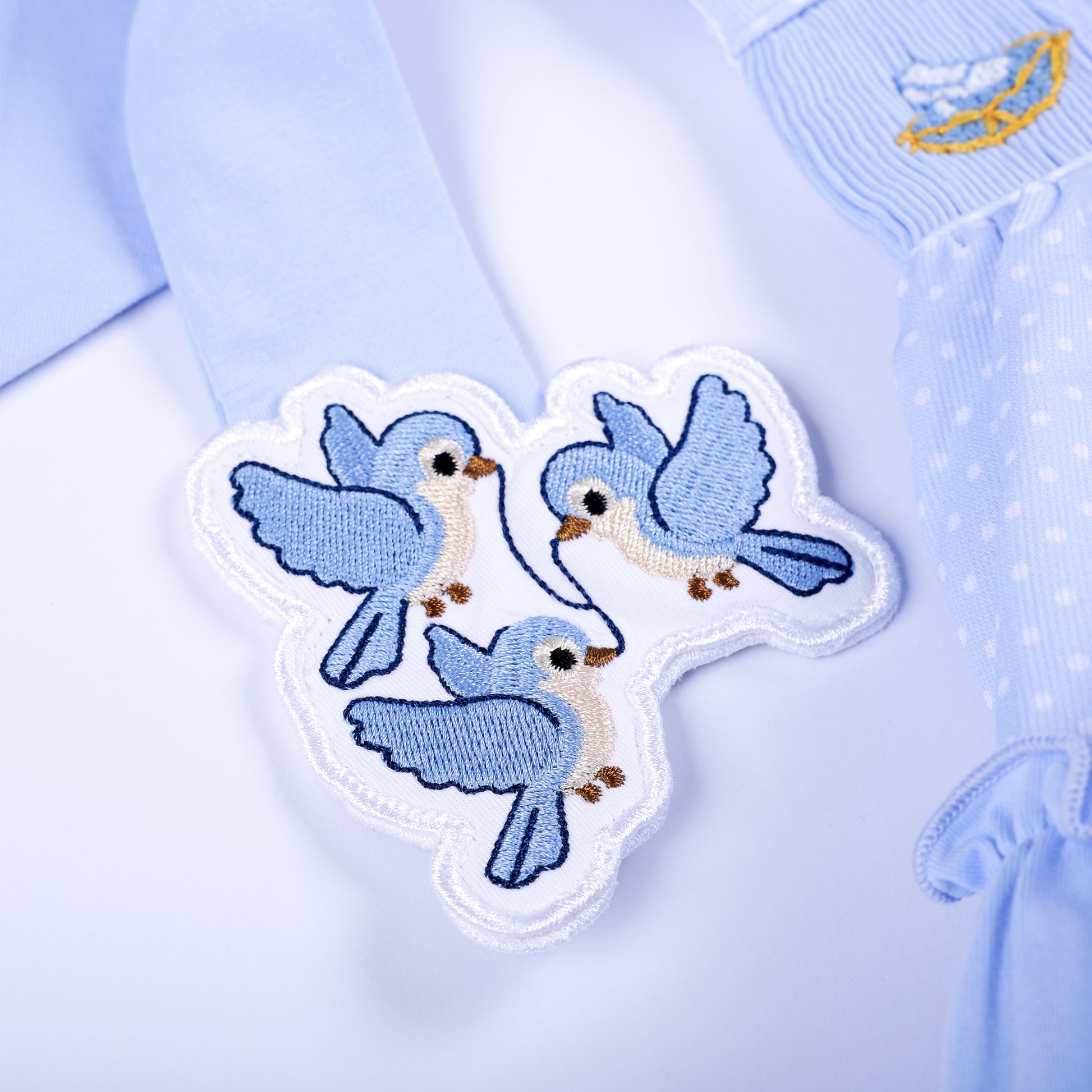 Close-up of hand embroidered blue bird patches on shoulder straps of Cinderella hand smocked clothing set.