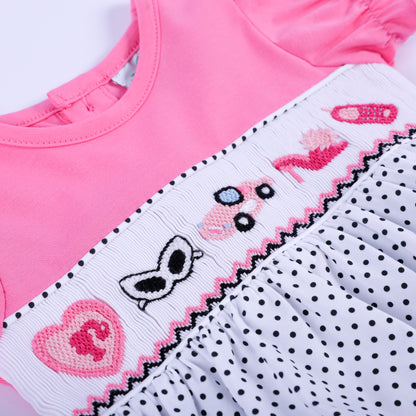 Macro shot of hand-smocked chest panel displaying pink hand-embroidered fashion accessories on polka dot bubble.