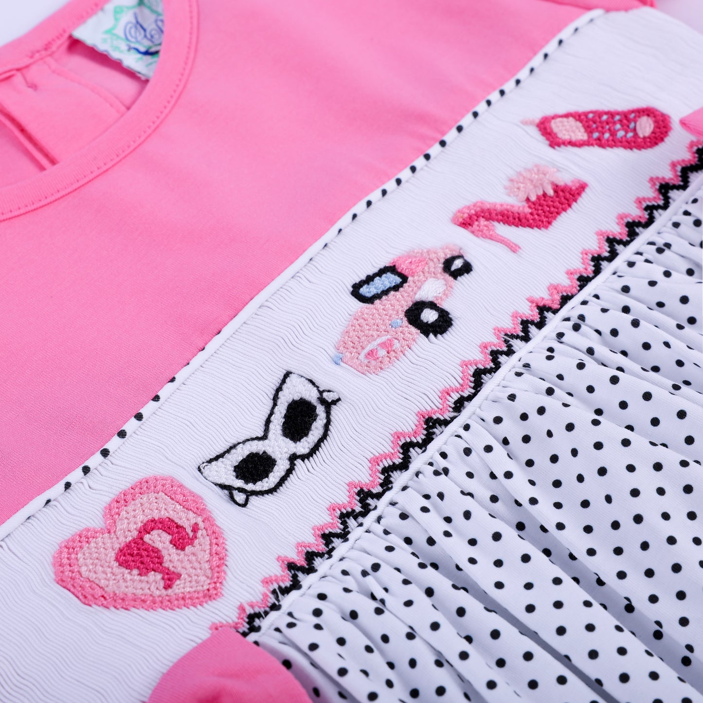 Angle view showing hand embroidered sunglasses car shoe and heart details on girls smocked pink dress.