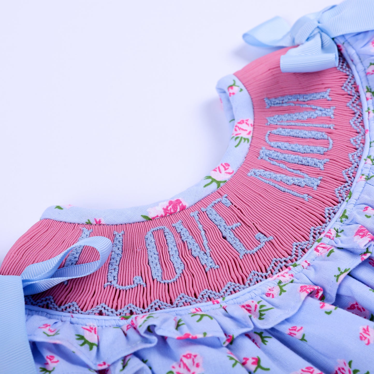Detailed view of hand embroidered I Love Mom lettering on pink smocked yoke of floral baby girl bubble.