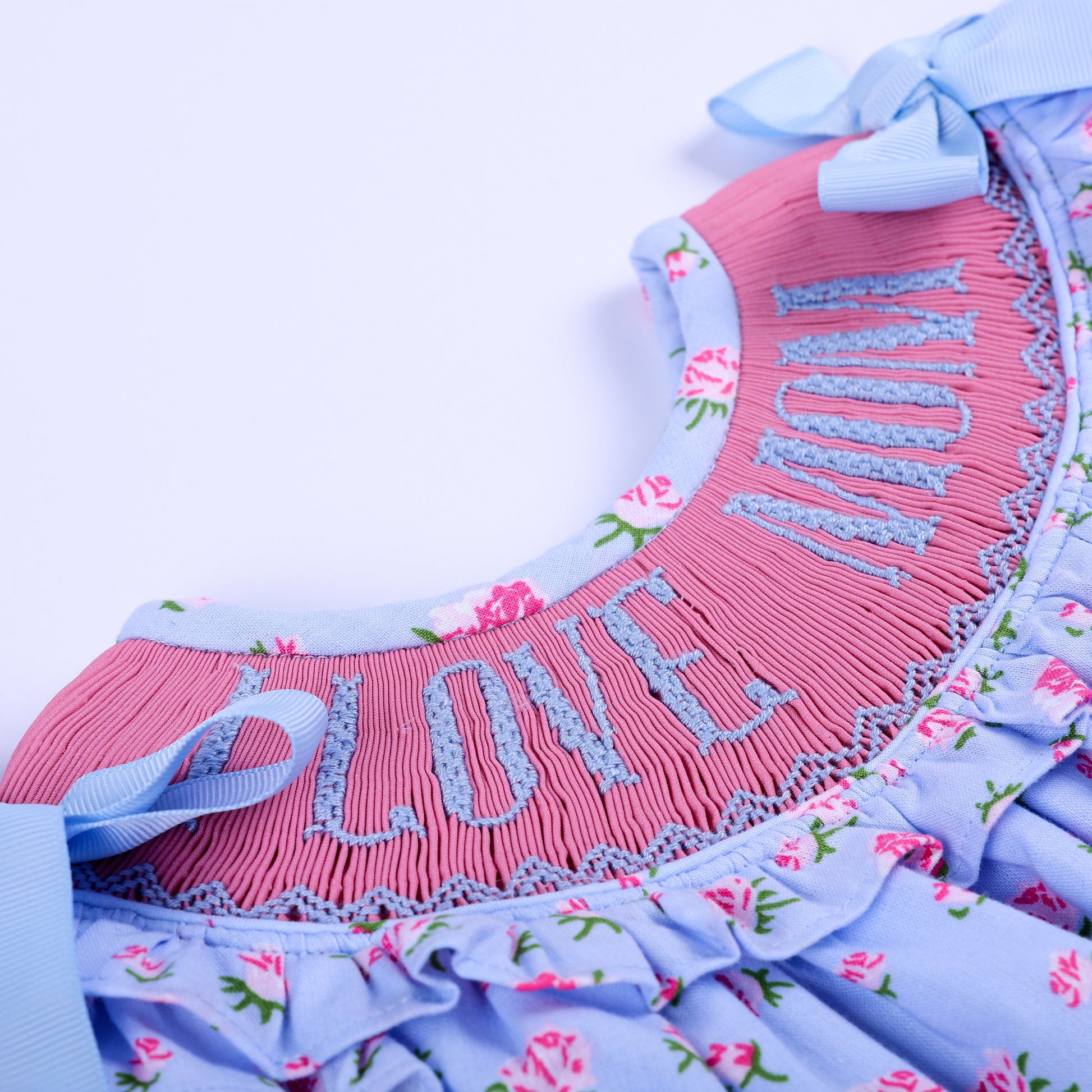 Detailed view of hand embroidered I Love Mom lettering on pink smocked yoke of floral baby girl bubble.