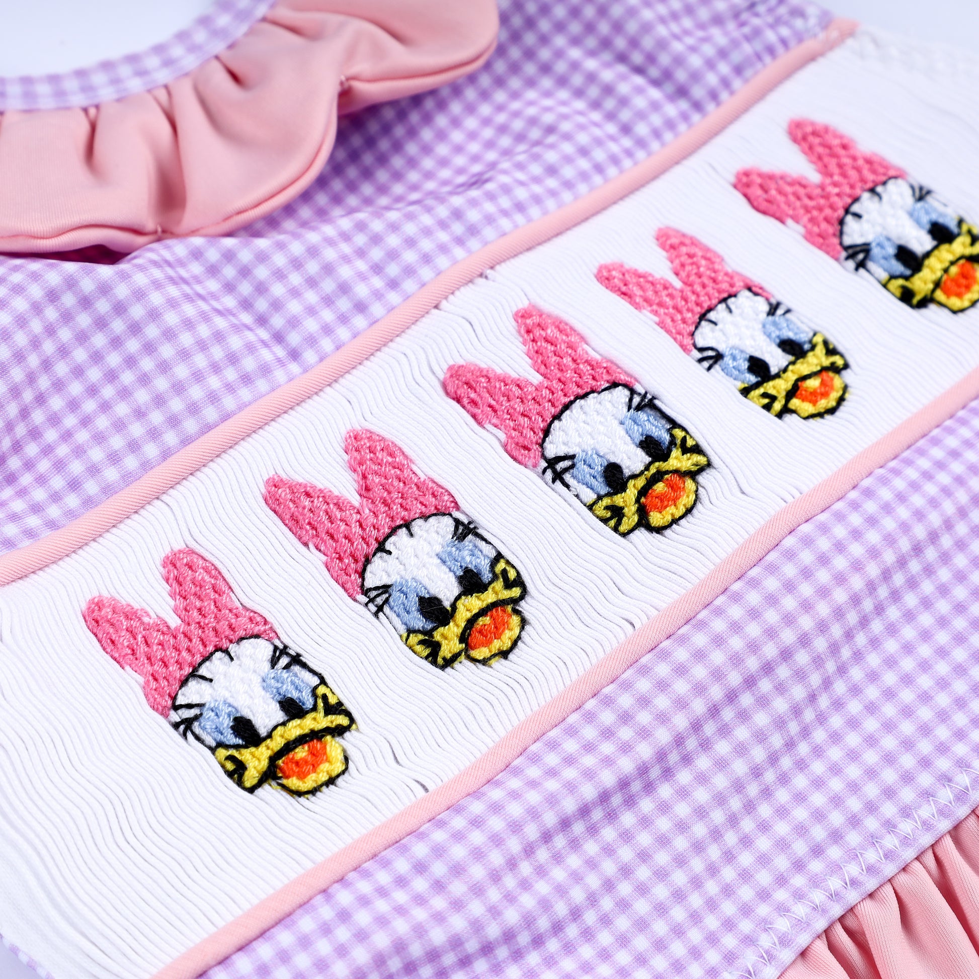 Detailed shot of hand-embroidered lady duck motifs on hand-smocked white panel of purple swimsuit top.