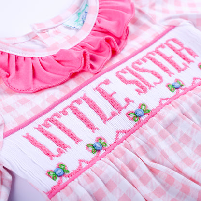 Macro detail of pink hand smocked embroidery reading Little Sister with floral accents on gingham sleep sack.
