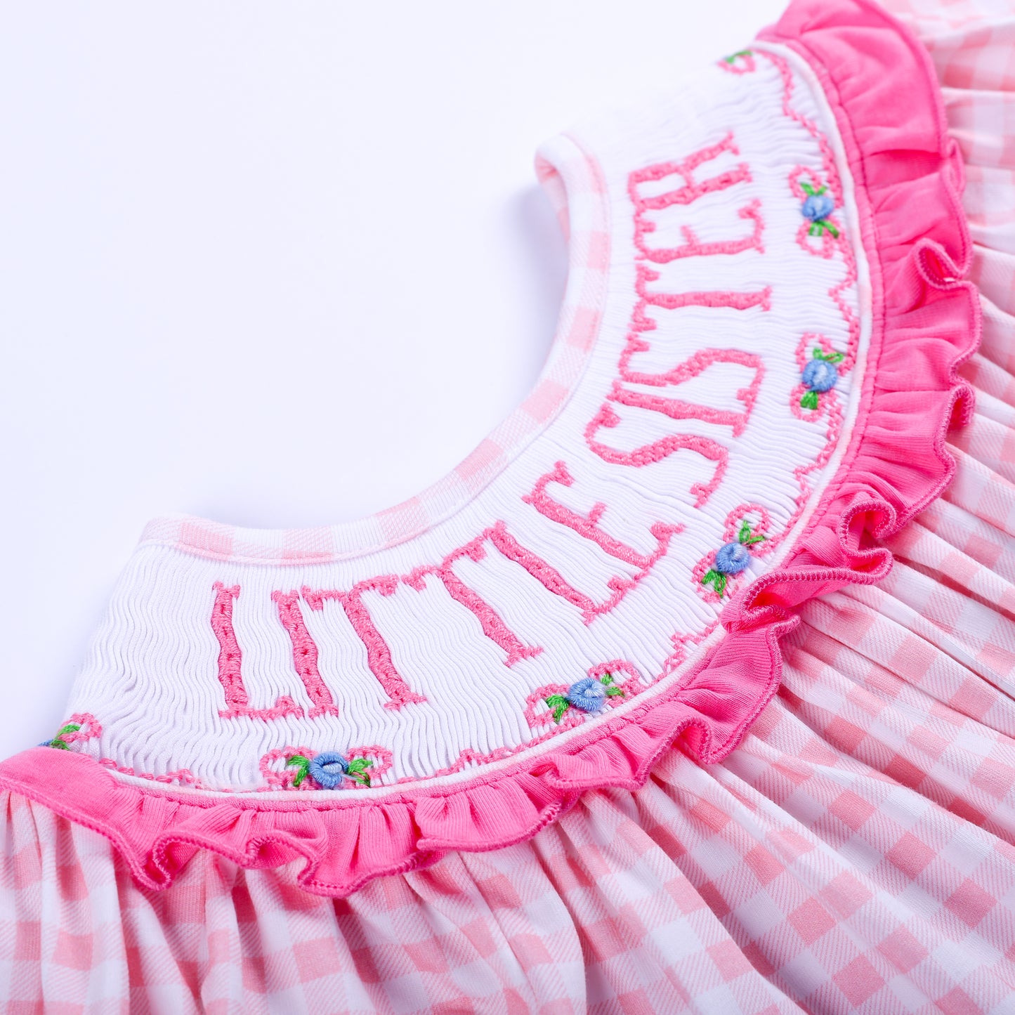 Macro close up of hand embroidered Little Sister text and floral details on smocked pink gingham bubble collar.