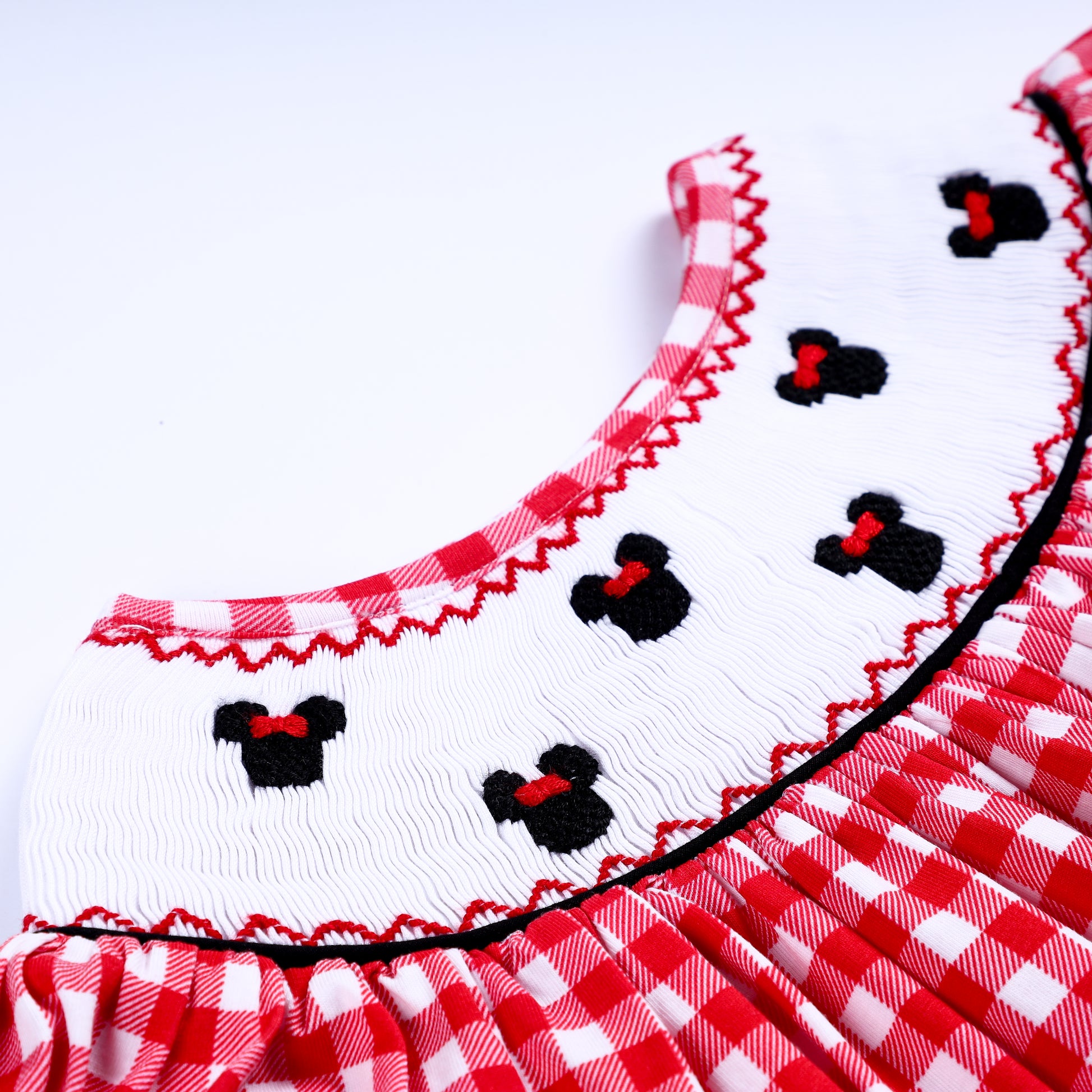 Close-up of hand embroidered black mouse motifs on the white smocked collar of a girls red gingham dress.