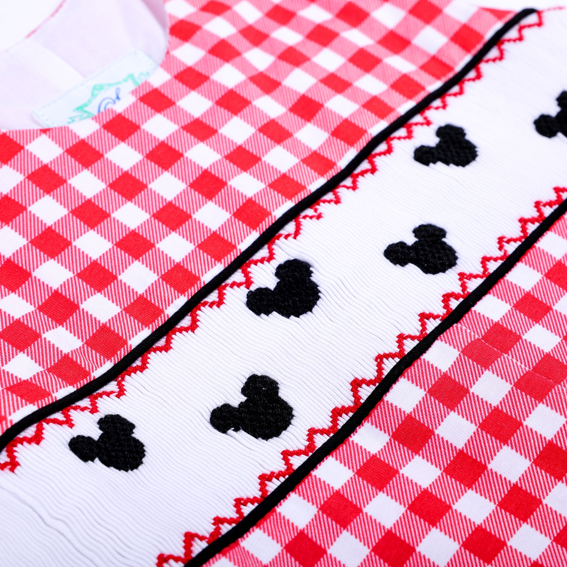 Detailed shot of hand embroidered black mouse shapes on white smocking trim of a red gingham boys jon jon outfit.