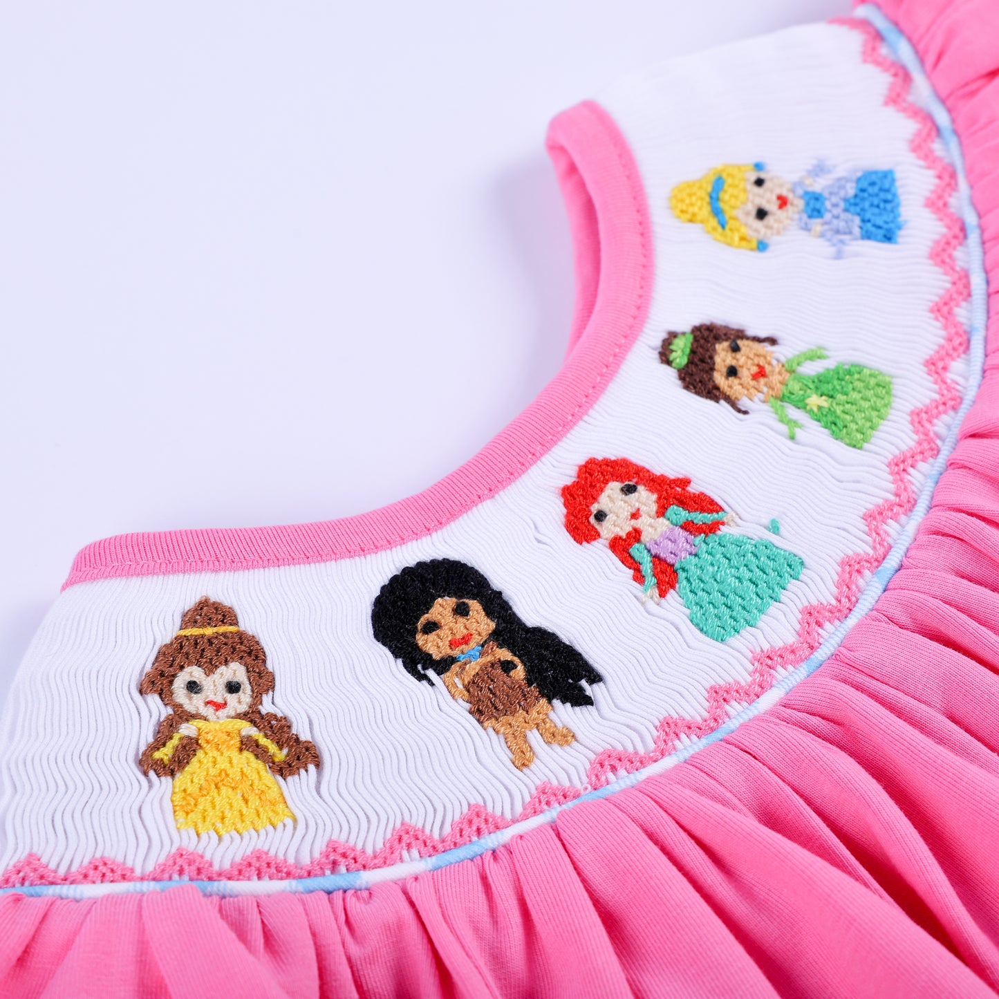 Close-up of hand-embroidered princesses on white smocked neckline of pink flutter-sleeve baby girl top.