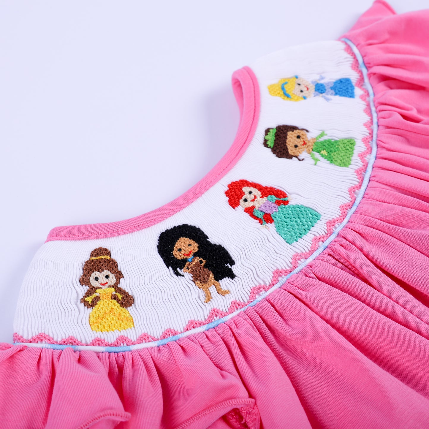 Angled detail shot of hand-smocked yoke featuring intricate embroidered fairy tale princesses on pink knit fabric.