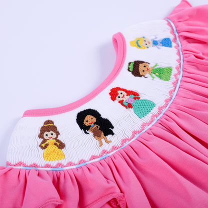Angled detail shot of hand-smocked yoke featuring intricate embroidered fairy tale princesses on pink knit fabric.