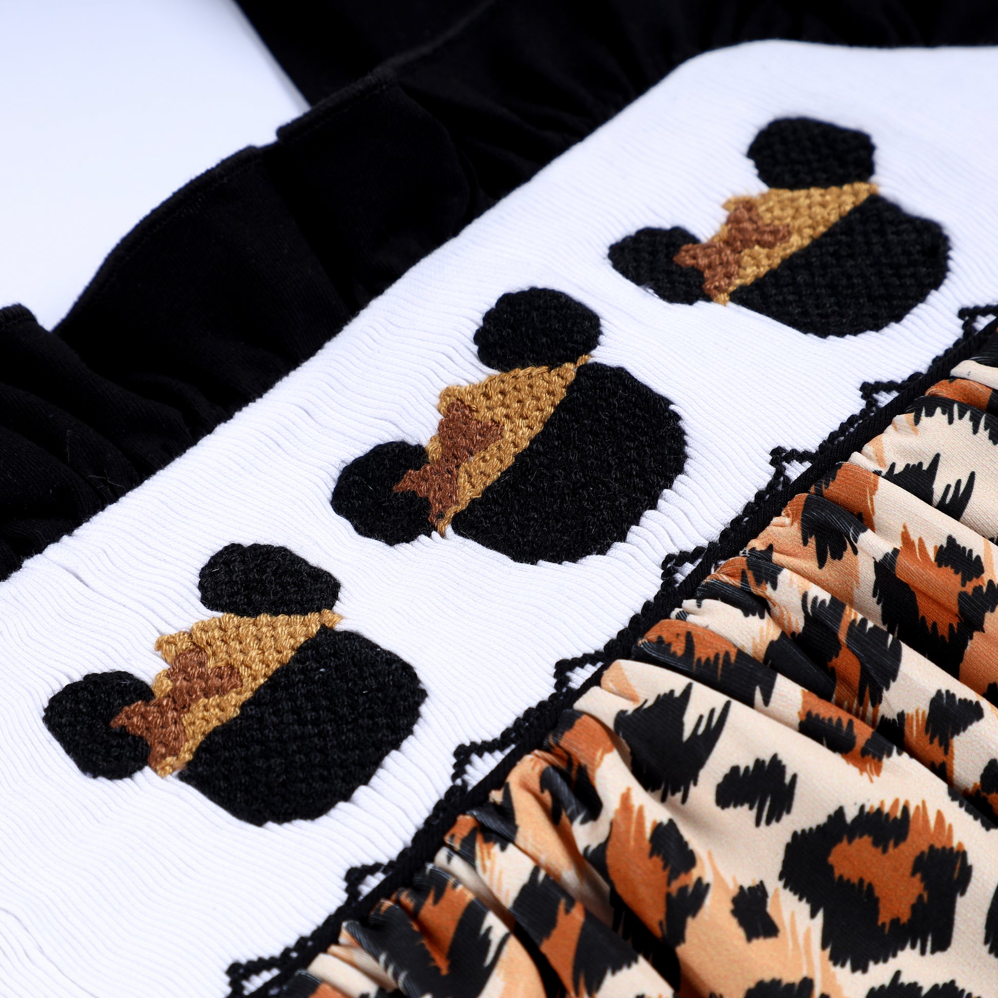 Detailed angled close-up of hand embroidered safari mouse heads on white smocked bodice with leopard printed fabric.
