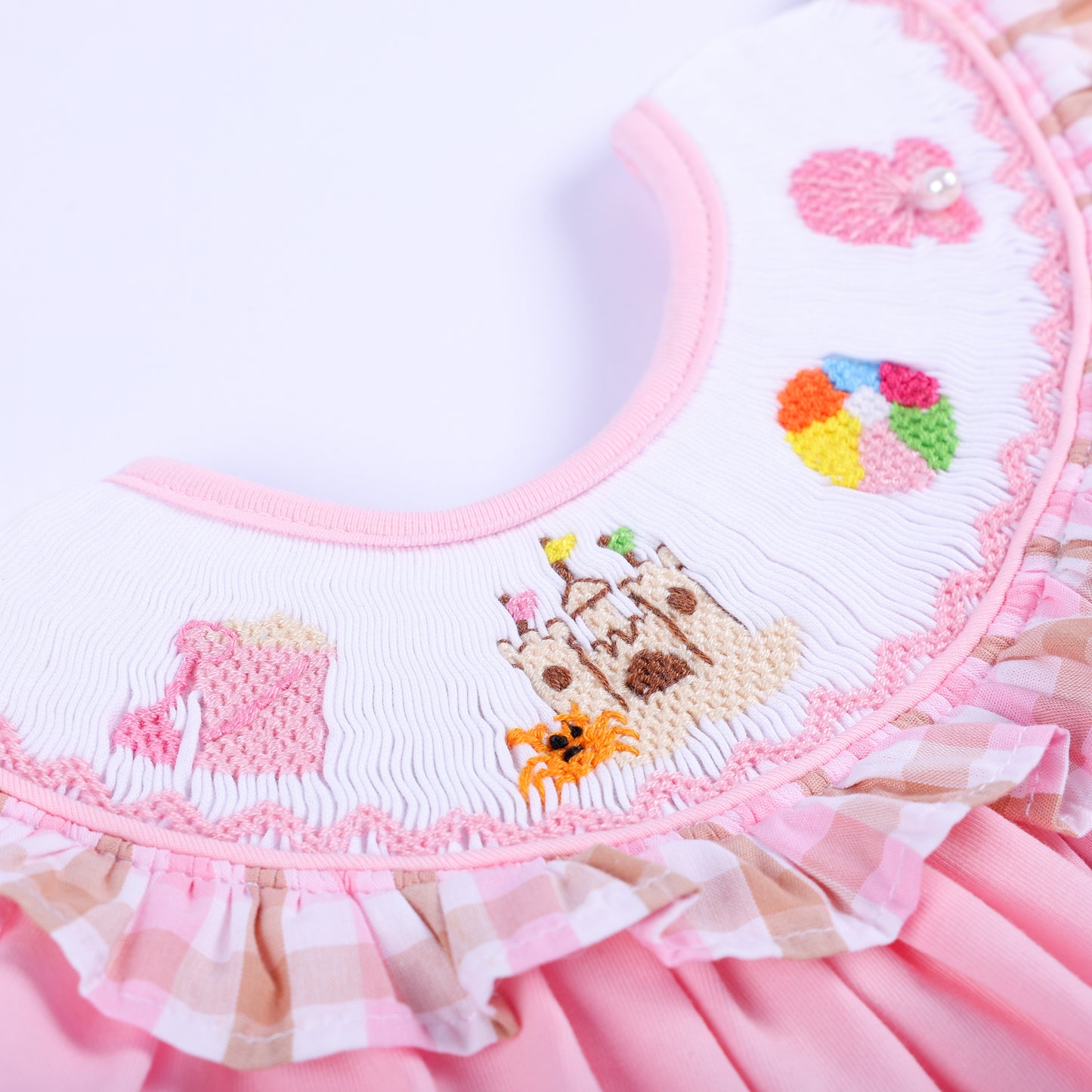 Detailed view of hand embroidered sandcastle, crab, and beach ball design on smocked white collar for baby top.